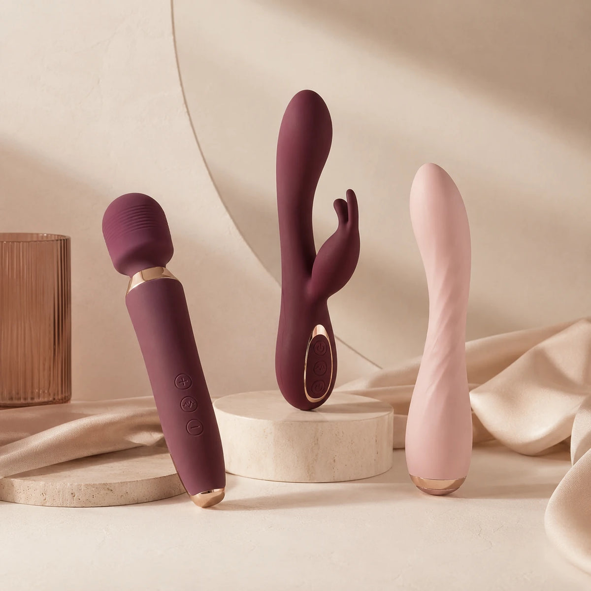 Trois vibromasseurs design prune et rose poudré présentés sur un décor champagne.